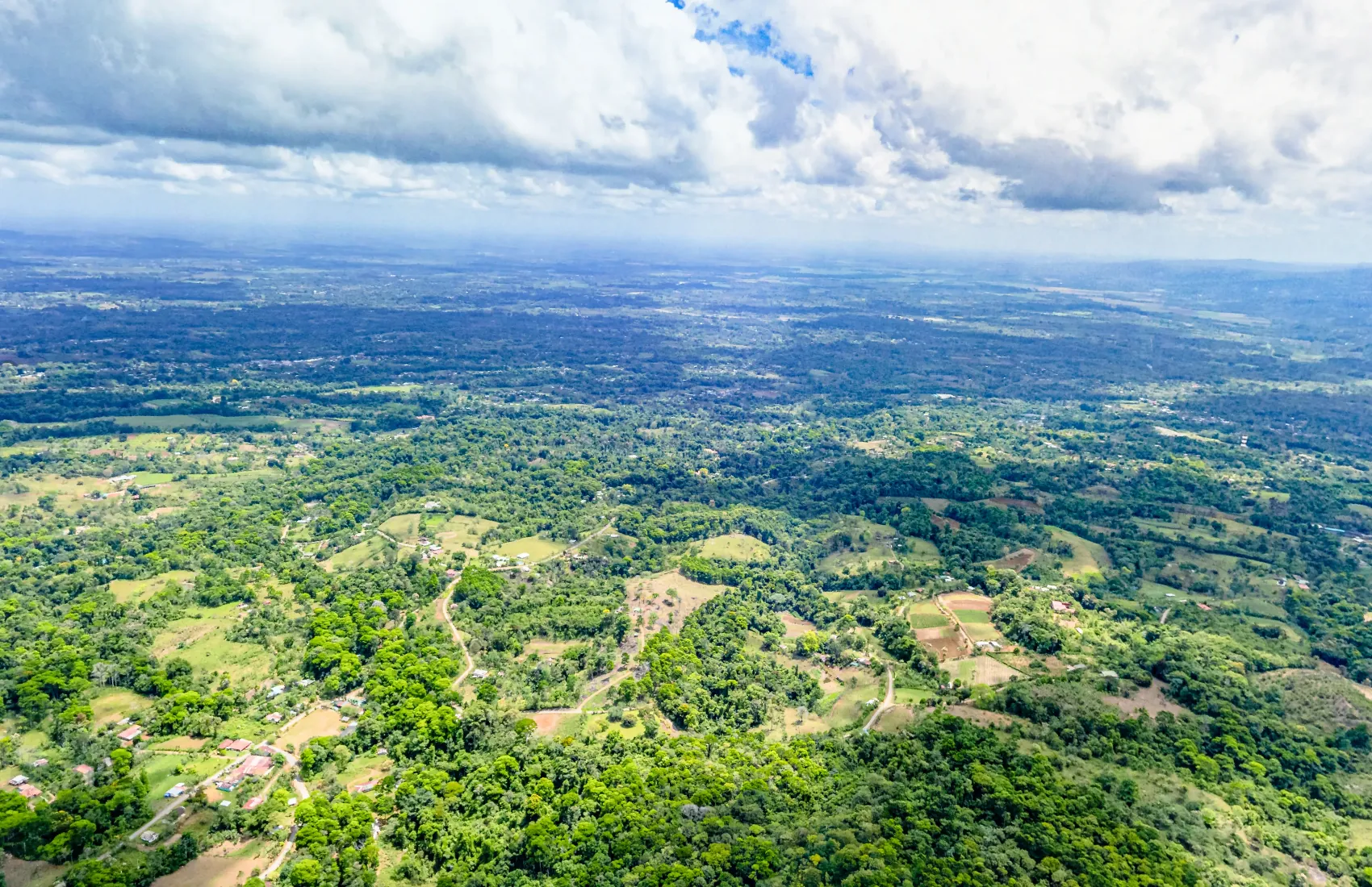 Drone view over forested foothills toward the green northern plains of San Carlos, Costa Rica